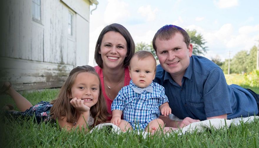 Dr. Nathan Corn with his family, lying on the grass in front of an old white outbuilding